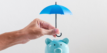Hand holding a tiny blue umbrella over a blue piggy bank.2
