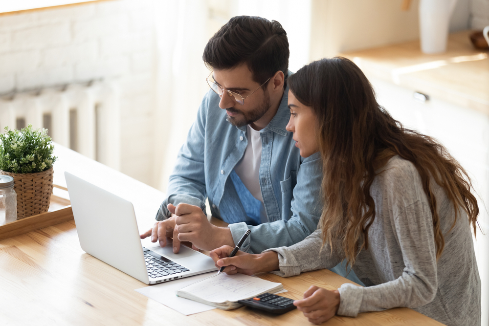 Couple looking together at a laptop. Women is taking notes and using a calculator.