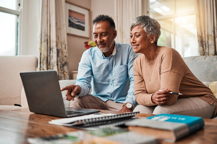 Senior age couple looking at a laptop together while sitting on a couch.