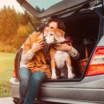 Woman sitting holding her dog in the trunk of her hatchback vehicle.