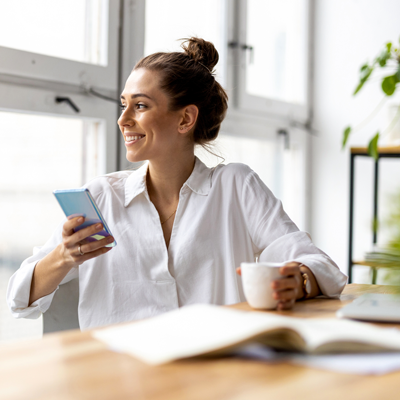 Woman sits at desk with coffee holding her phone.