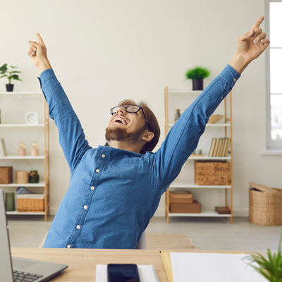 Man at desk with laptop celebrating by pointing both arms and hands into the air
