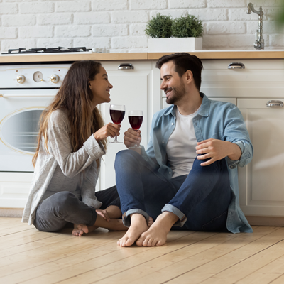 Young couple sit on kitchen floor in a new home smiling and sharing glasses of wine