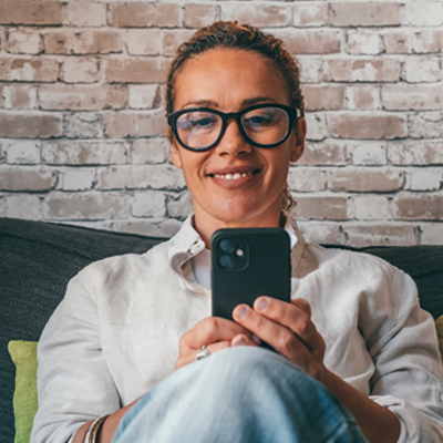 Woman sits on couch looking at her phone.
