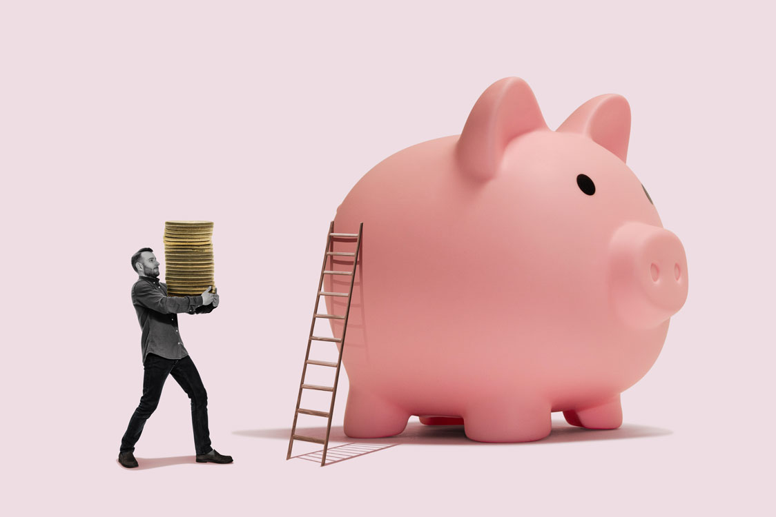 Tiny man carrying a stack of coins to deposit in a giant pink piggy bank