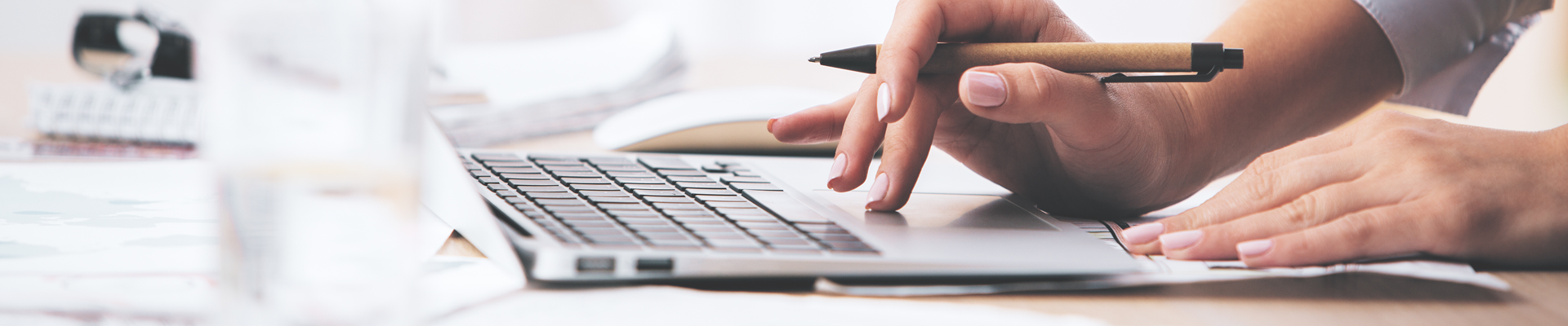 Person holding pen while using the mouse pad of a laptop to navigate