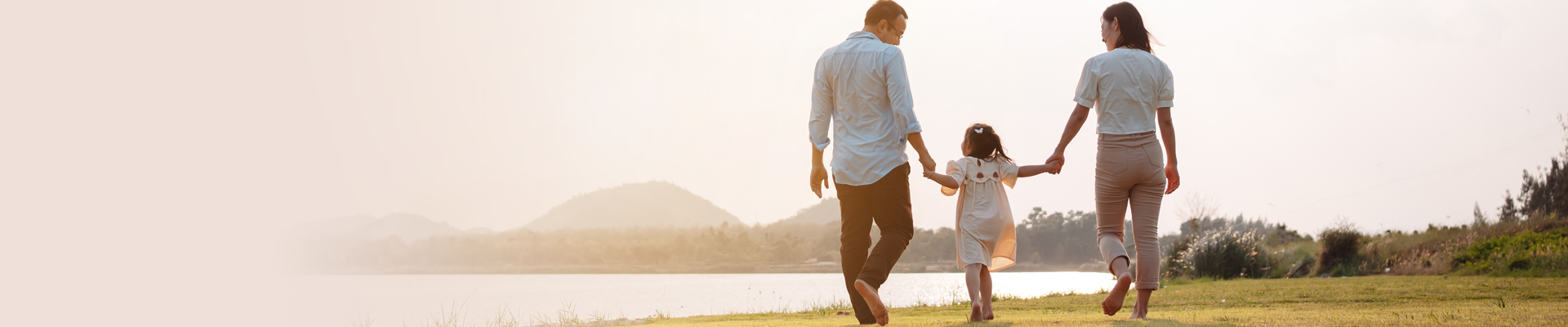 Couple holding hands with their young daughter walking along a lake