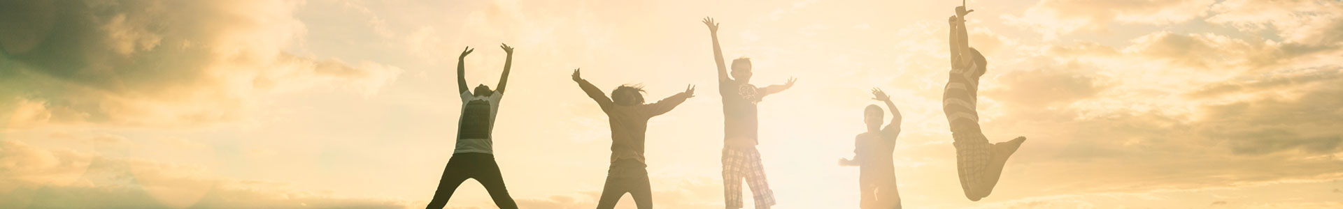Five young adults jumping in the air to celebrate against a background of the sun shining through clouds