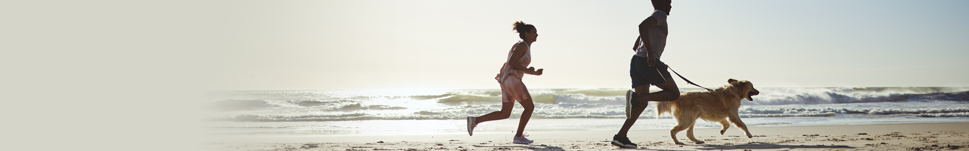 Father and daughter run along beach with the father holding their dog by the leash